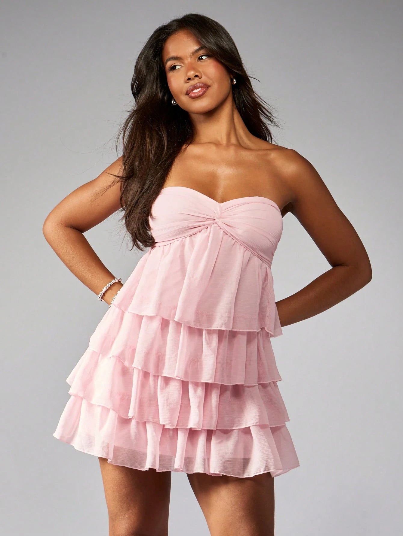 Elegant strapless mini dress with tiered ruffles, twist-front detail, and empire waist.